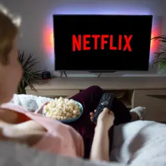 Kobieta z popcornem i pilotem przed telewizorem z logo Netflix.