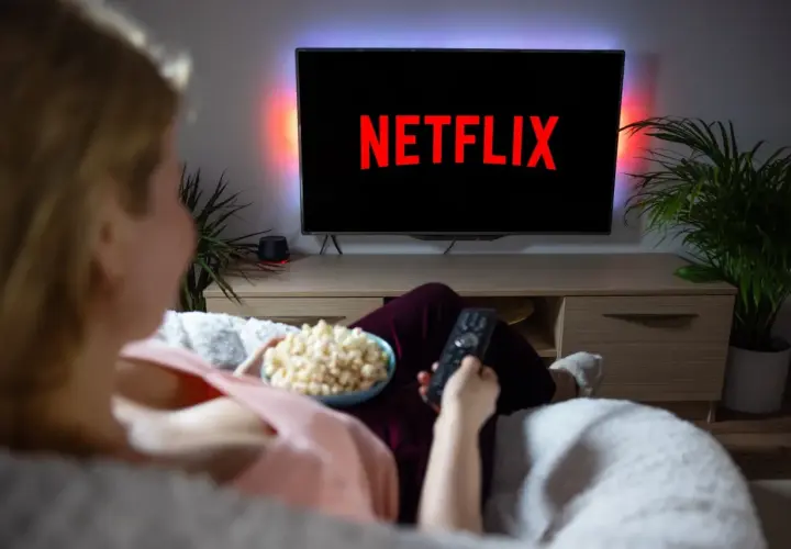 Kobieta z popcornem i pilotem przed telewizorem z logo Netflix.