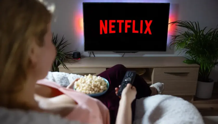 Kobieta z popcornem i pilotem przed telewizorem z logo Netflix.