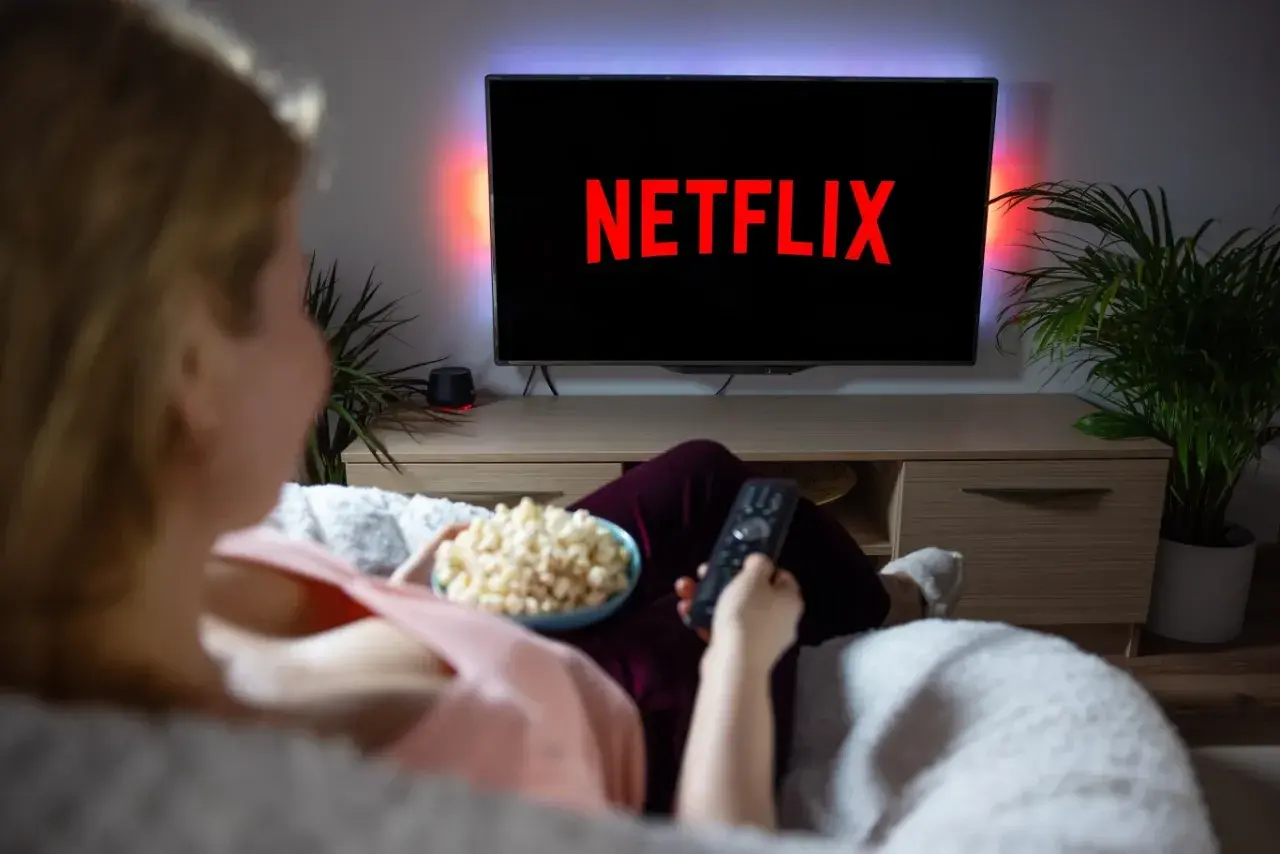 Kobieta z popcornem i pilotem przed telewizorem z logo Netflix.